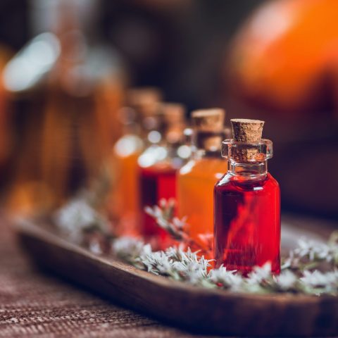 Bottles filled with red and orange essential oils on wooden board. Aromatherapy relax concept