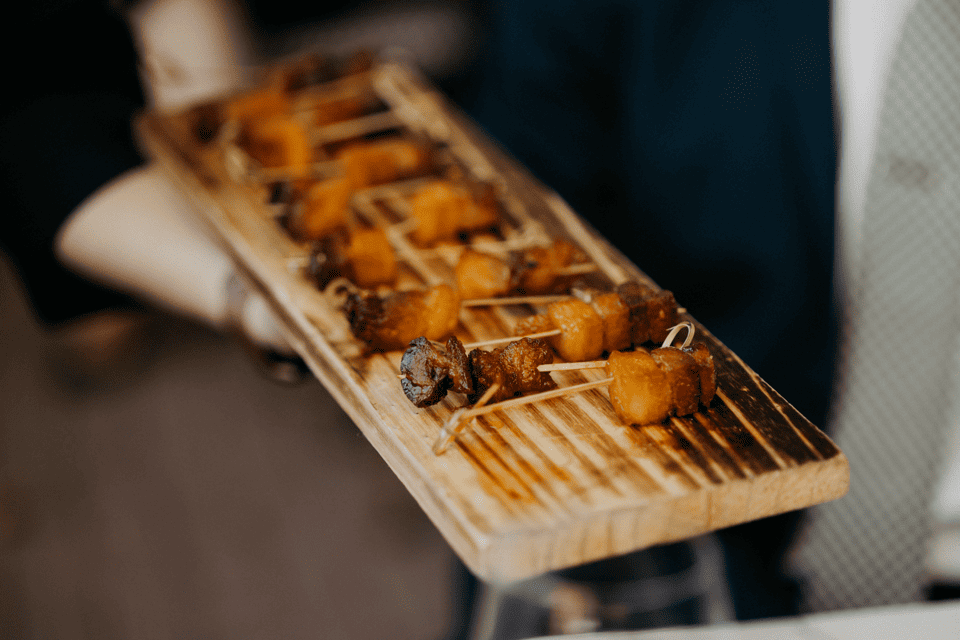 A wooden serving board holds several skewered appetizers, featuring cubes of glazed meat and vegetables. The skewers are neatly arranged in rows, suggesting a formal dining or catering setting. 124 on Queen Hotel and Spa | Hotel & Spa Niagara-on-the-lake | 1 (855) 988-4552