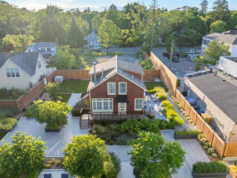 Aerial view of a two-story brown house with white trim, surrounded by a landscaped yard, patio areas, green trees, and adjacent buildings in a suburban neighborhood. 124 on Queen Hotel and Spa | Hotel & Spa Niagara-on-the-lake | 1 (855) 988-4552
